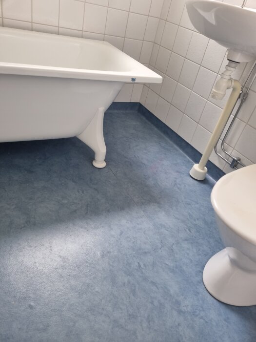 Blått badrumsgolv invid badkar och toalett, gränsar till kaklade väggar. Diskuteras ifall golvmattan kan bytas utan att påverka kaklet.