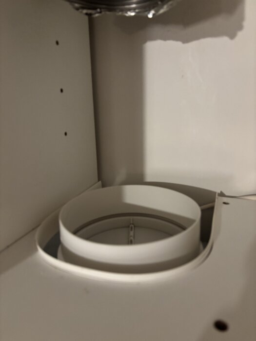 Vit plastadapter för köksfläktens utlopp, utan gummipackning, visas ovanpå utloppet som ska anslutas till spirorör.