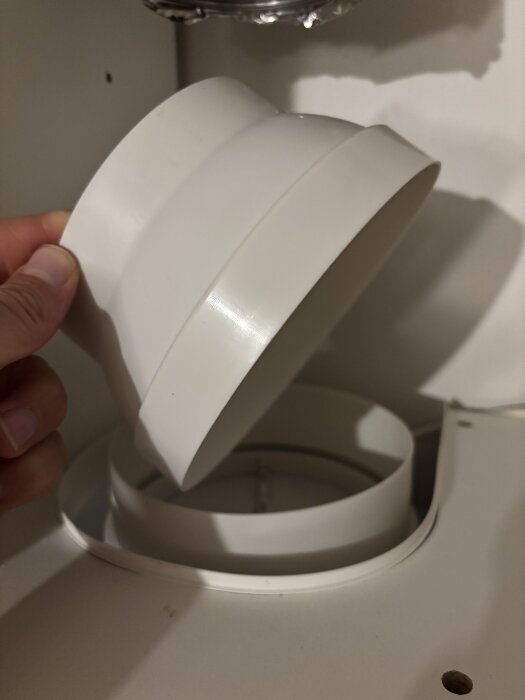 En vit plastadapter för köksfläkt hålles över en öppning. Adaptern saknar gummipackning och är avsedd för en utgång med 150 mm i diameter.
