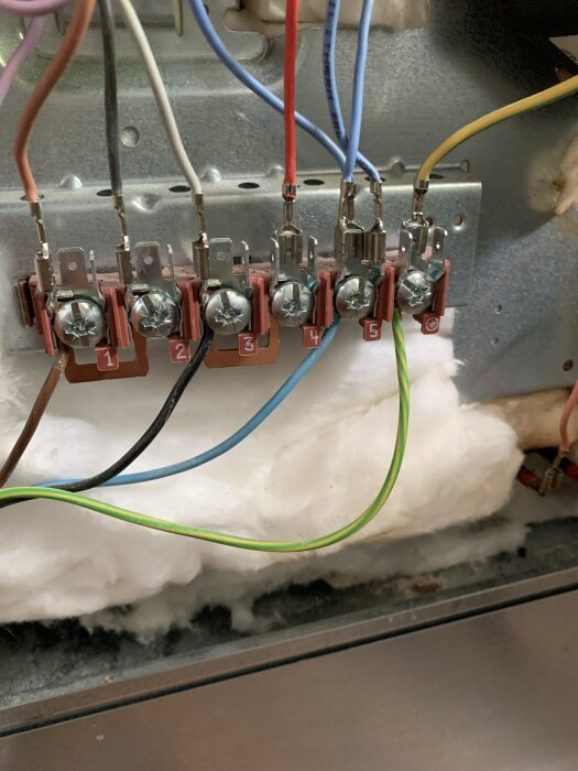 Elektrisk kopplingsplint med sex kablar i olika färger anslutna, mot en bakgrund av isoleringsmaterial.