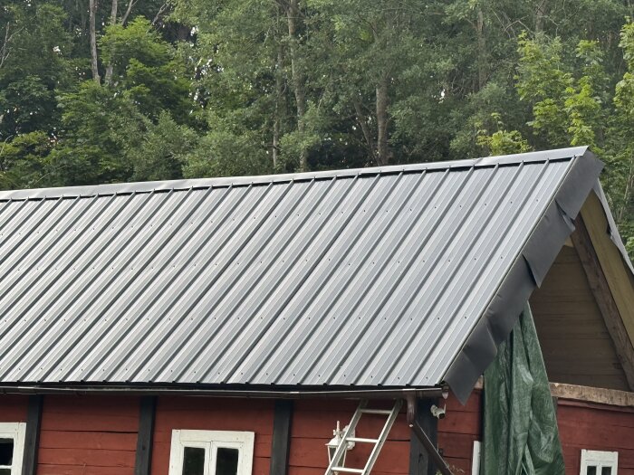 Plåttak på en röd träbyggnad visar nockplåt installerad utan stöd, med papp synlig där takplåt inte når nock.