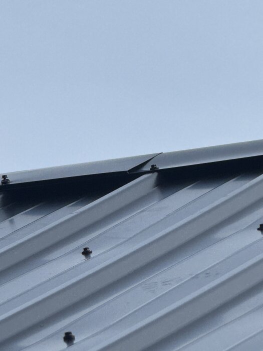 Plåttaket med nockplåt som är böjt för hand; takplåten når inte helt upp till nocken, synlig papp under nockplåten.