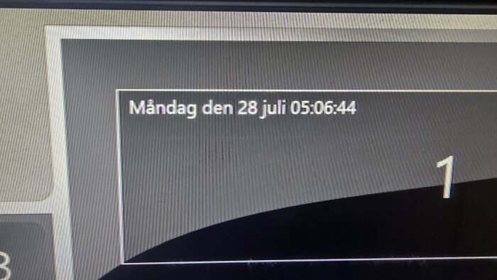 Skärmbild av en dator med texten "Måndag den 28 juli 05:06:44" och siffran 1 i nedre högra hörnet mot bakgrund av en grå panel.