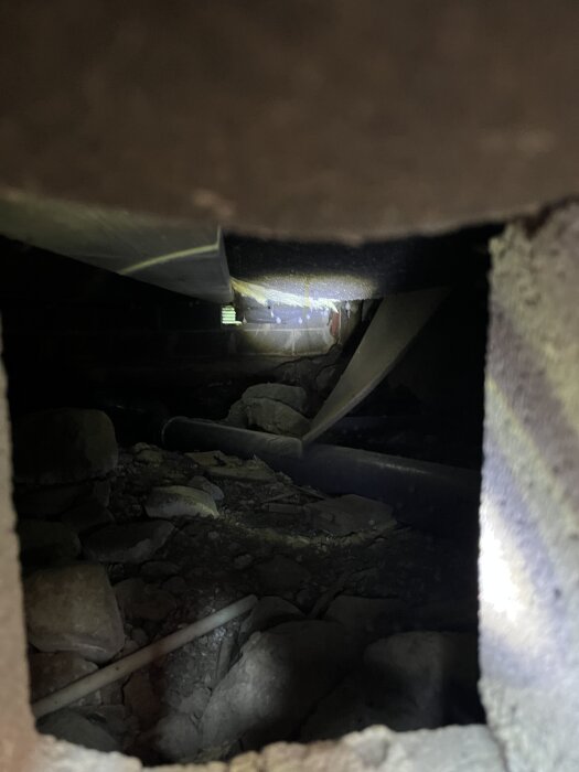 Vy under tillbyggnad med lossnade skivor som håller fast isoleringen och synliga stenar, rör och mörker.