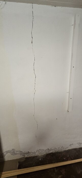 Spricka i en vit källarvägg från golvet och uppåt.
