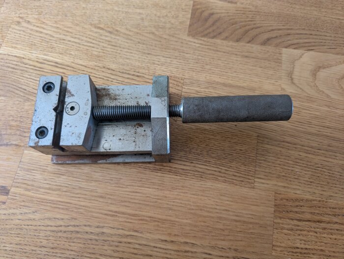 Ett maskinskruvstycke i metall på ett träbord, med en märklig inskription "Manchester United" undersida.