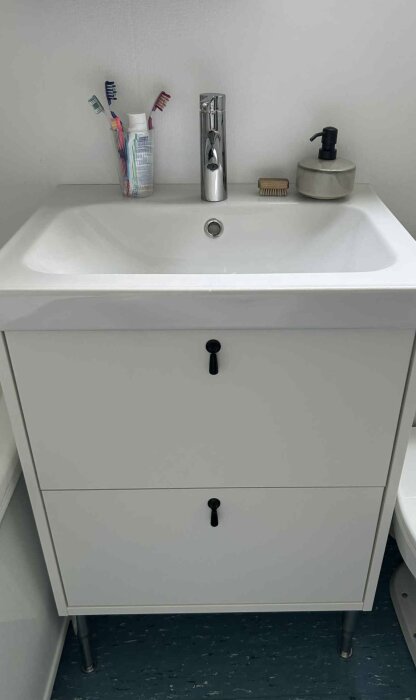Vit badrumskommod med handfat, kran, tandborstar och tvålautomatik. Nyinstallerad utan läckage.