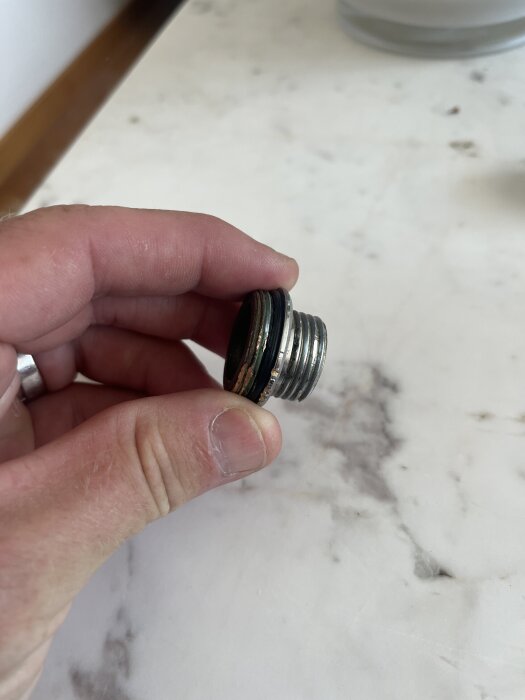 En hand håller en metallkonverter med gänga, avsedd för att byta dimension från 1 tum till 1/2 tum i ett duschsystem.