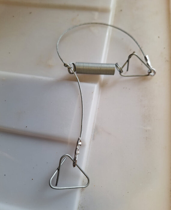 Trådformad fälla med fjäder och metalltråd från gammal husvagn mot vit bakgrund.