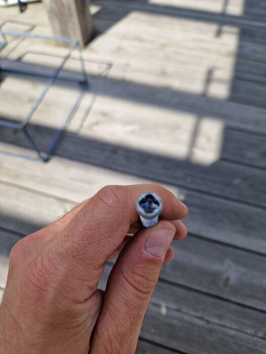 Skruv med huvudet format som en fyrklöver hålls mellan fingrarna med en trätäckt uteplats i bakgrunden.