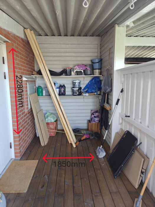 Inngangsparti med treplanker, maling og verktøy mot bølgeblikktak. Merkede mål på vegg og gulv. Planer for å bygge vegg med dør for oppbevaring.