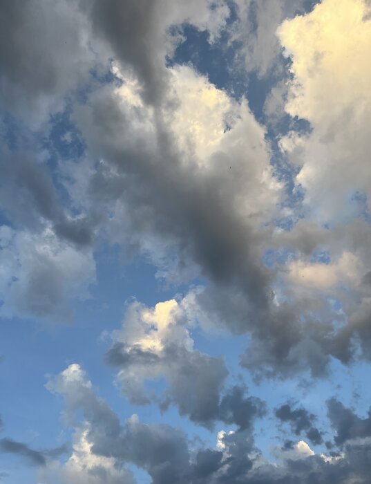 Vacker himmel med spridda moln i olika gråtoner mot en blå bakgrund.