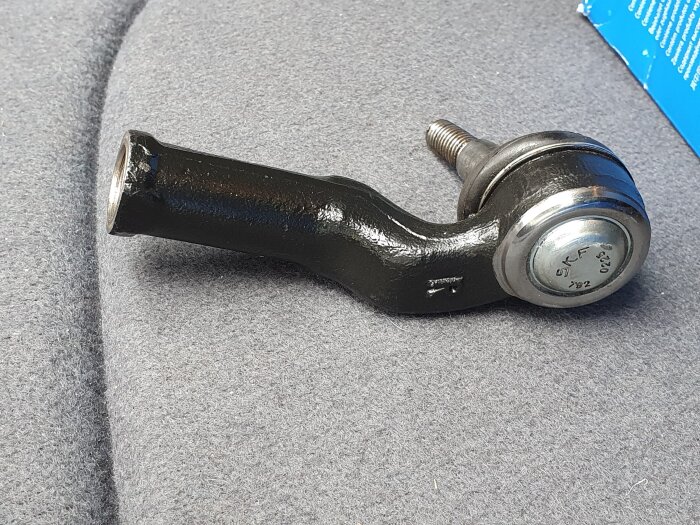 En styrled yttre vänster med märkning "SKF" ligger på ett grått tygunderlag.