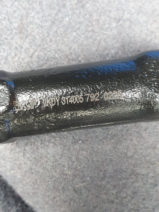 Närbild av en svart metallstång med ingraverad text "SKF VKDY 314005 792 0285" på en grå bakgrund.