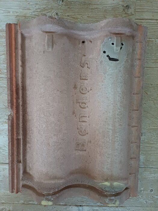 Trasig takpanna från Benders med sprickor och en ihålig del, märkt av vittring och missfärgning, visar tecken på vattenläckage.