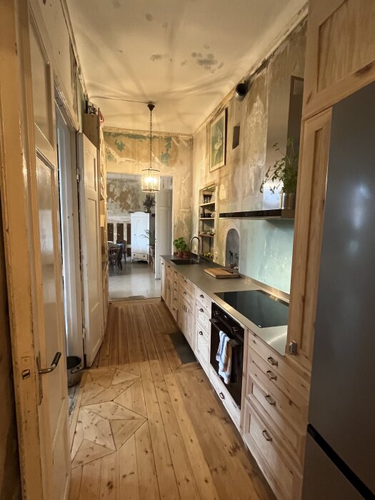 Renoverat kök med trägolv, träskåp och modern inredning, halvklart med väggar som behöver fixas, syns ljus från taklampa och konst på vägg.