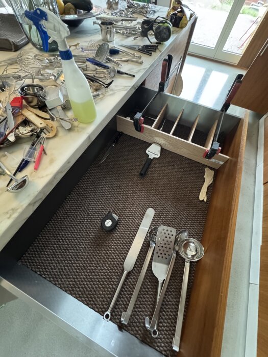 Öppen kökslåda med delare och köksredskap, verktyg på bänk. Projekt för att organisera lådor i progress.