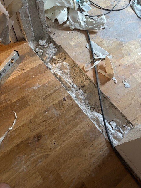 Ojämt golv vid nytt dörrhål i ett sovrum, med synligt hål i golvet och byggmaterial spritt omkring.