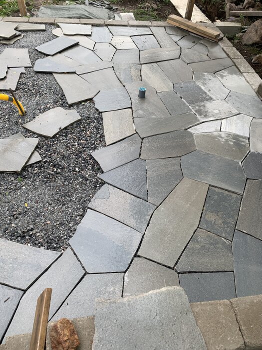 Oregelbundet skiffergolv under konstruktion för ett utekök, med många snitt och olika storlekar på skifferplattorna.