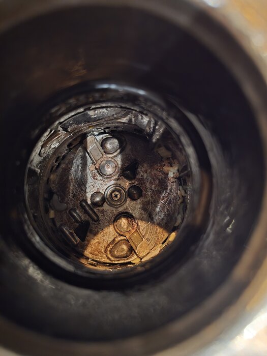 Inuti en avfallskvarn med synlig skruv och skiva, där monteringen är problematisk p.g.a. saknad metall vid skruvfästet.