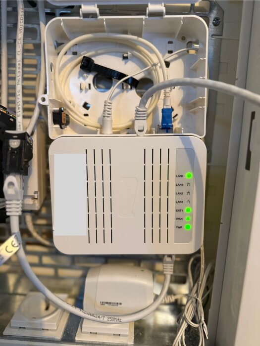 Öppen fiberomvandlare med kablar anslutna till olika portar, inklusive LAN-portar och EXT1, med indikatorlampor som lyser grönt.