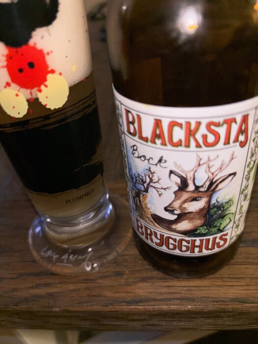 Flaska med etikett från Blacksta Brygghus "Bock" och ett glas öl på ett bord.