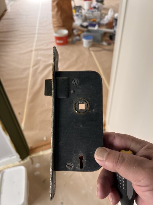 Gammal låskista från en lägenhet, daterad 1939, hålls i en hand. Bakgrunden visar verktyg och material för renovering.