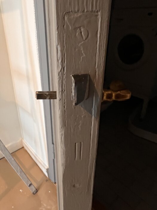 En gammal dörr med synlig låskista och nyckel eller handtag. Dörren är delvis öppnad och visar slitage på karmens målningsfinish.