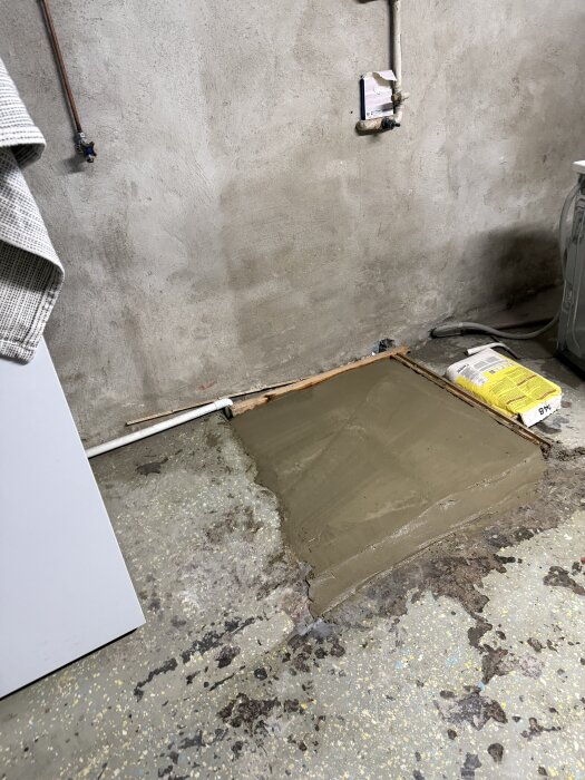 Gjuten betongförlängning av en pannplatå i en tvättstuga med grovt golv och en säck byggmaterial bredvid.