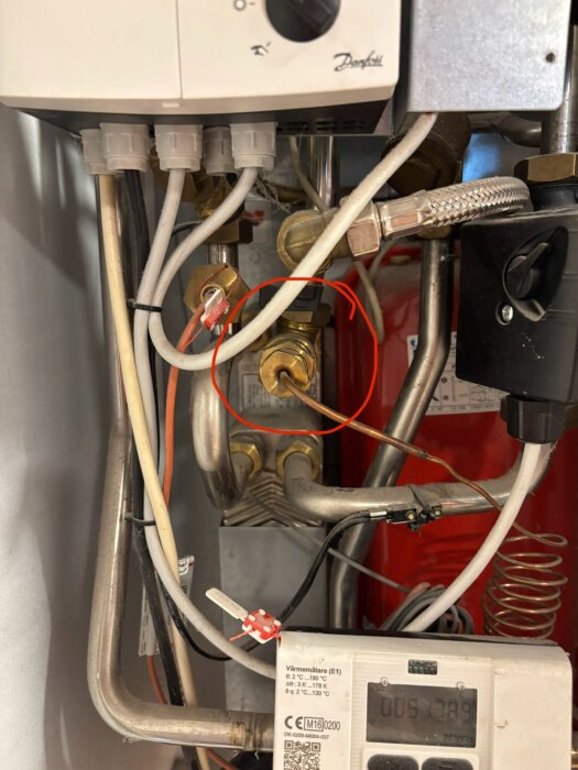 Fjärrvärmecentral med markerad ventil där ett kopparrör går in, omringad av ledningar och rör.