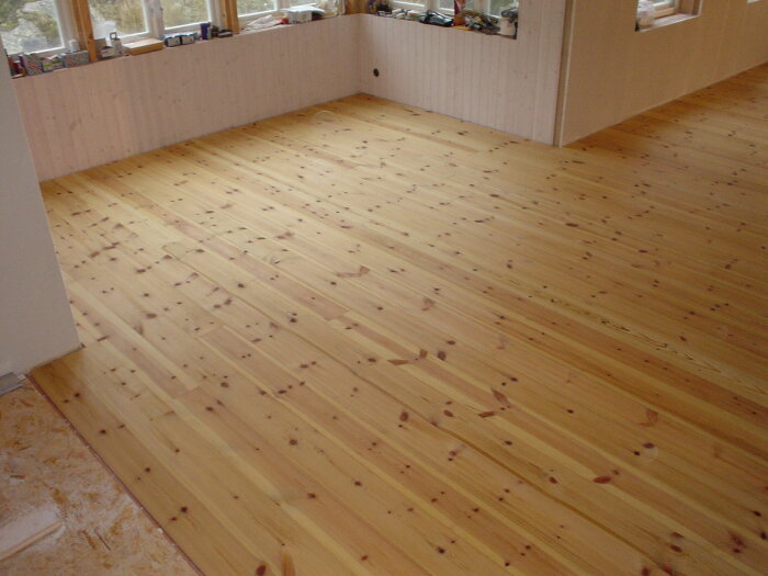 Nylagt och behandlat trägolv i ett rum med stora fönster, visar ljus och varm nyans efter lutning och oljning.