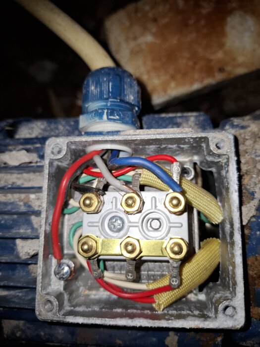 Elektrisk motoranslutning med flera färgade kablar och skruvanslutningar i en blå motorhölje, märkning synlig.