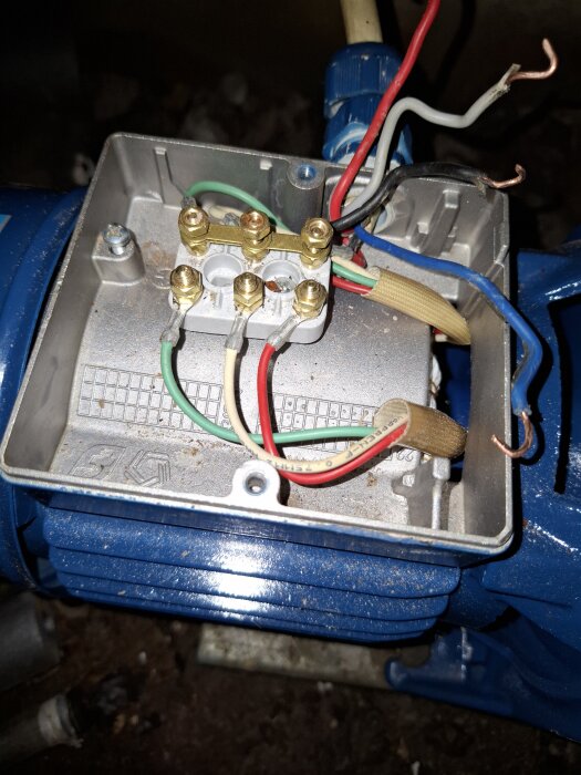 Närbild på öppnad terminalbox på en blå motor, med exponerade kablar anslutna till terminaler.