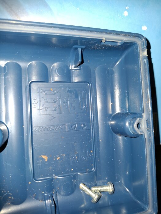 Blå plastlåda med två skruvar och märkningar på insidan mot en blå bakgrund.