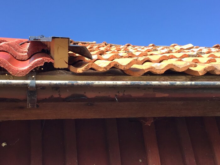 Plåt mellan tak med betongpannor och tegelpannor, synliga glipor vid regeln och felmonterad plåt över fotbrädan. Potentiell vattenläcka.