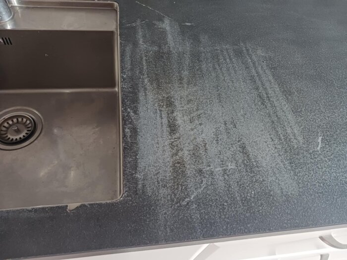 Bänkskiva vid diskho med tydliga skurmärken och missfärgningar, troligen orsakade av starka rengöringsmedel.