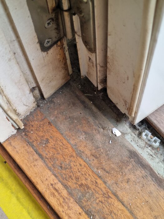 Smutsig dörrkarm och golvlist med damm och smuts vid ett gångjärn.