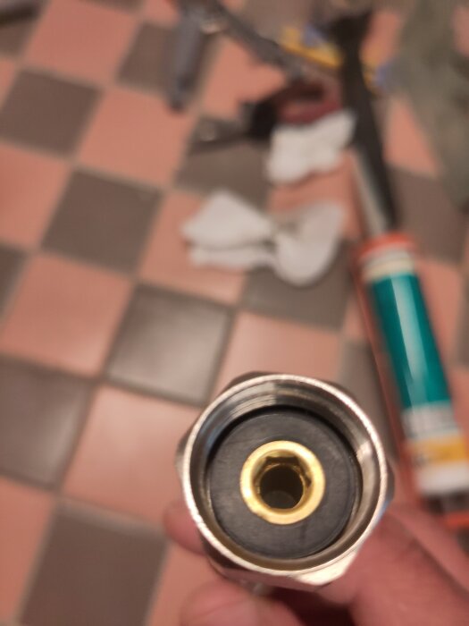 Vinkelkoppling med synlig packning; rördelens ända visas med svart packning och mässingsinfattning, suddig verktygsmiljö i bakgrunden.