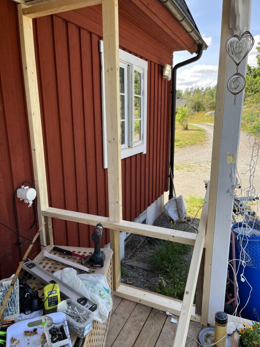 Rött hus fasad med vitmålat fönster; verktyg och träreglar i förgrunden för byggprojekt.