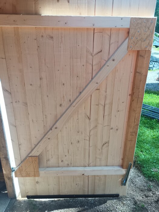 Trädörr med snedställda träbalkar och plåtvinkel, del av hemmagjord lösning för garage.