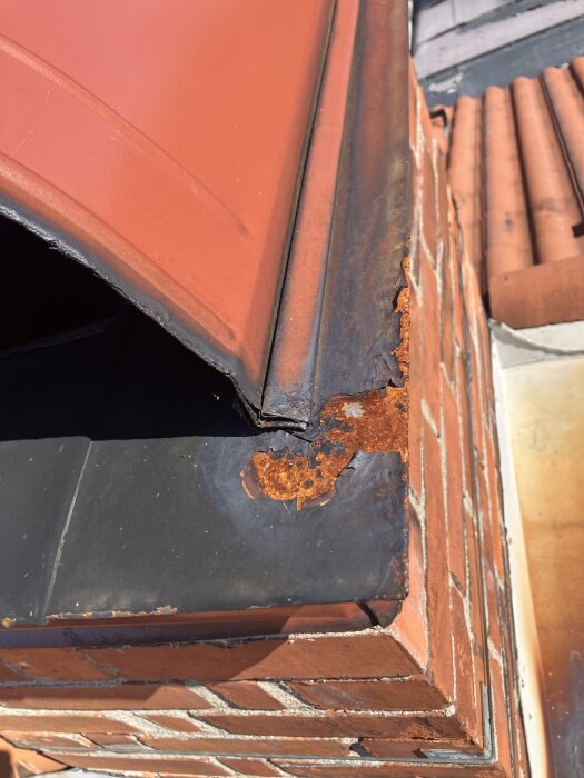 Rostig plåt omger en tegelmurad skorsten med avflagad färg, särskilt runt kanterna. Detta visar ytrosten som diskuterades.