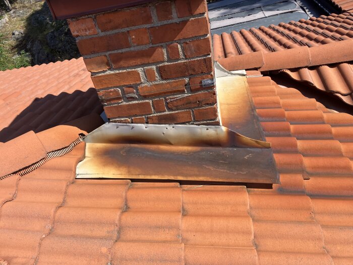 Plåtdetaljer runt skorstenen med ytrost på tegeltak.