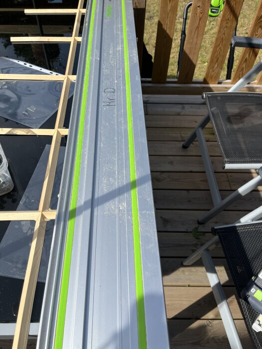 Sänksåg med styrskena på ett trädäck bredvid ett byggprojekt, stolar och verktyg syns.