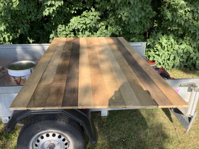 Nybyggd trädörr på släpvagn, klar för målning med svart färg. En hink grundolja syns bredvid, i solig utomhusmiljö.