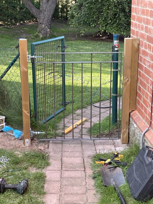 Grind provmonterad med verktyg som vattenpass och skruvmejsel runt om. Står på stenlagd gång vid ett tegelhus. Bakom syns ett staket.