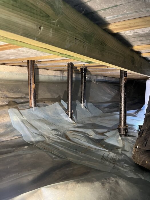 En krypgrund med golvbjälkar, stöttor och plastfolie på marken.