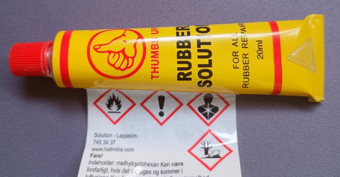 Gul tub med lösningsmedel för gummireparation, varningstext och symboler för brandfarlighet och miljörisk.