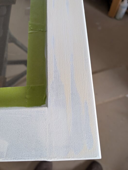 Närbild av ett vitmålat fönster med maskeringstejp och områden med genomslipade och missfärgade lackfläckar.