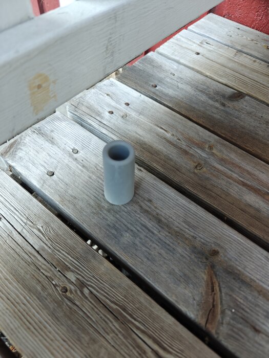 Grå cylinder på trätrall med röd vägg i bakgrunden.