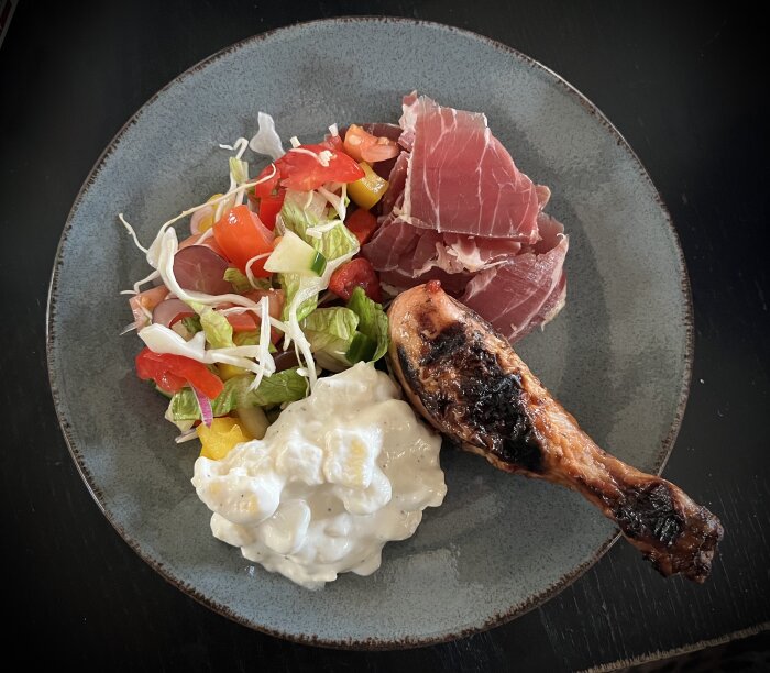 Tallrik med sallad, skinka, potatissallad och kycklingben.